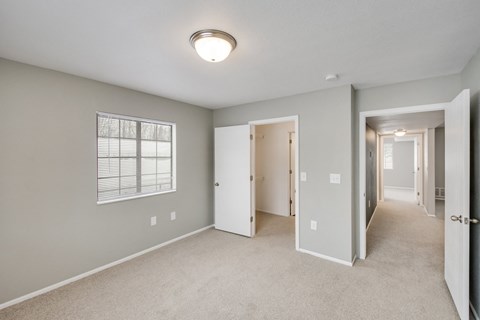 A spacious room with a carpeted floor and a window with blinds.