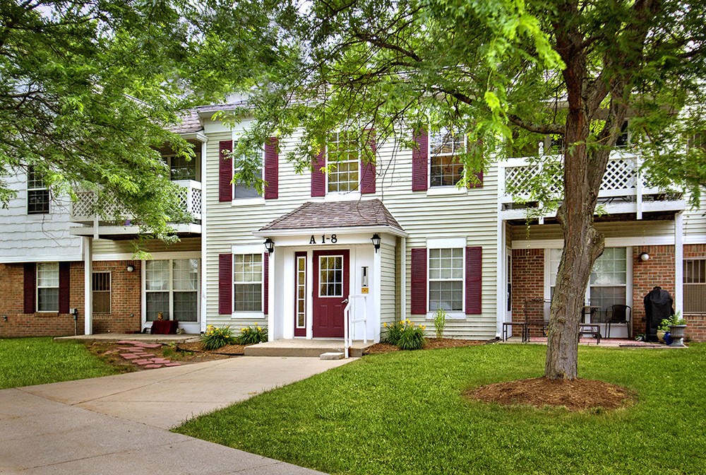 A white house with a red door and a tree in front.