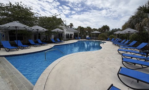 A large outdoor swimming pool surrounded by blue lounge chairs and umbrellas.