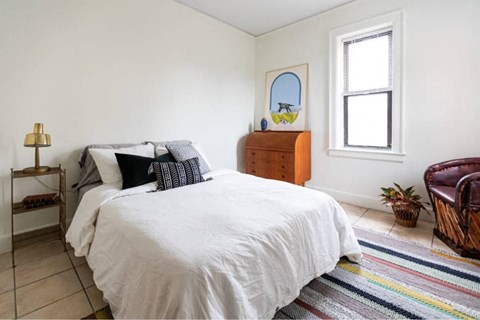 A bedroom with a white bed and a wooden dresser.