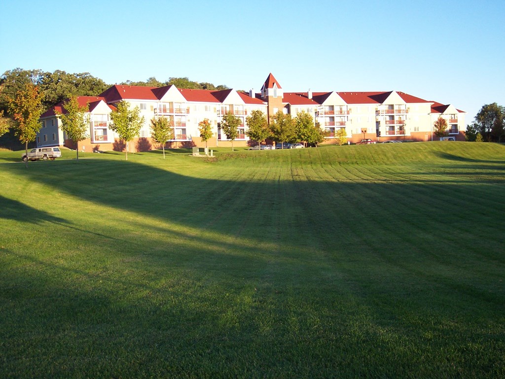 A large white building with a red roof sits in a grassy field.