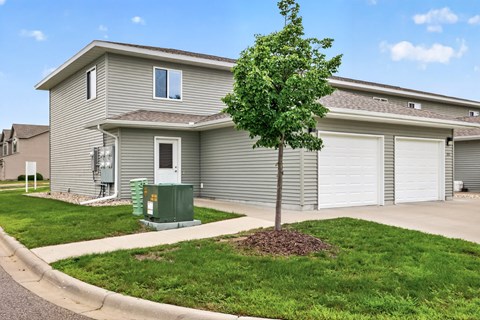 A tree in front of a grey house with a green utility box.