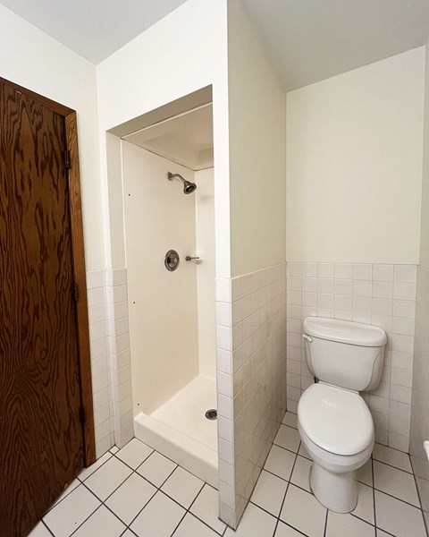 A white toilet in a small bathroom with a white tiled floor and walls.