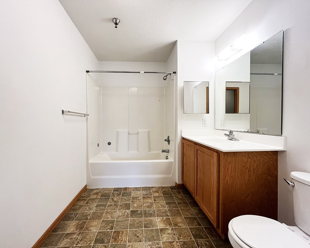 A bathroom with a white tub, brown tiles, and a white toilet.