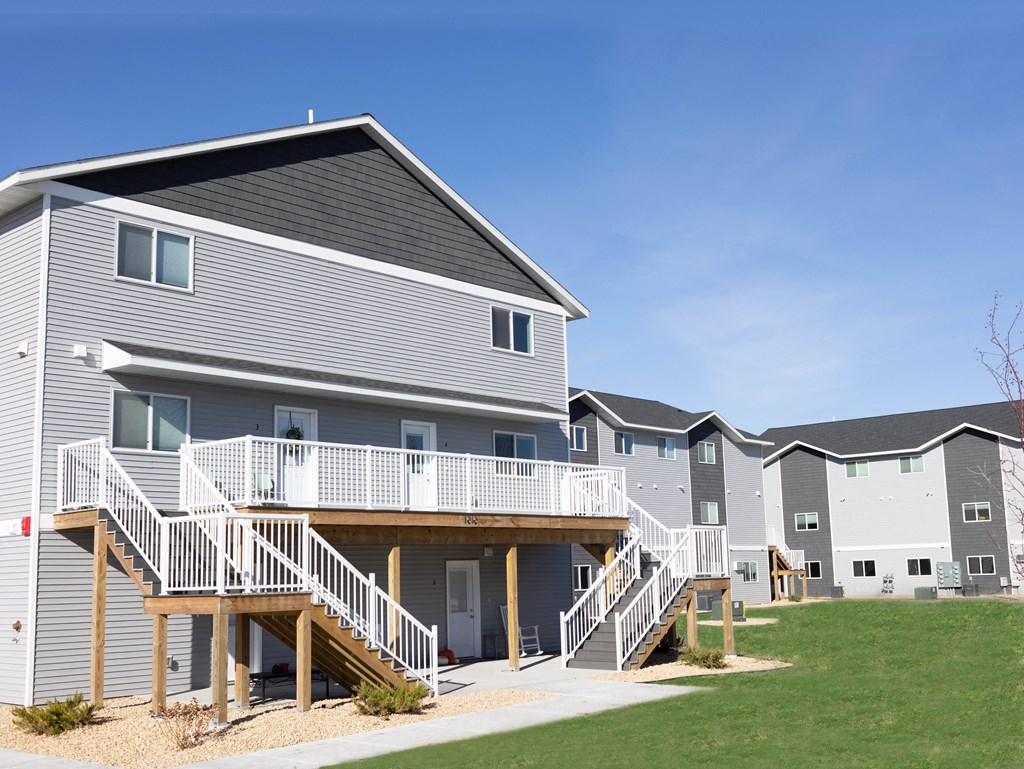 A grey and white apartment building with a balcony and stairs.