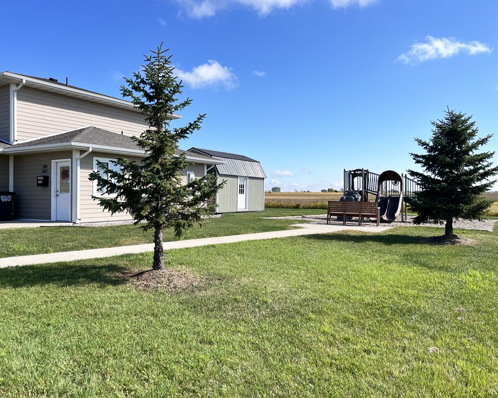 A playground with a slide and swings is located in a grassy area in front of a building.