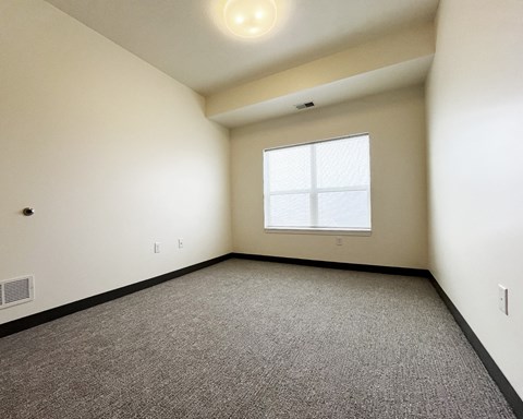 A room with a carpeted floor and a window with blinds.