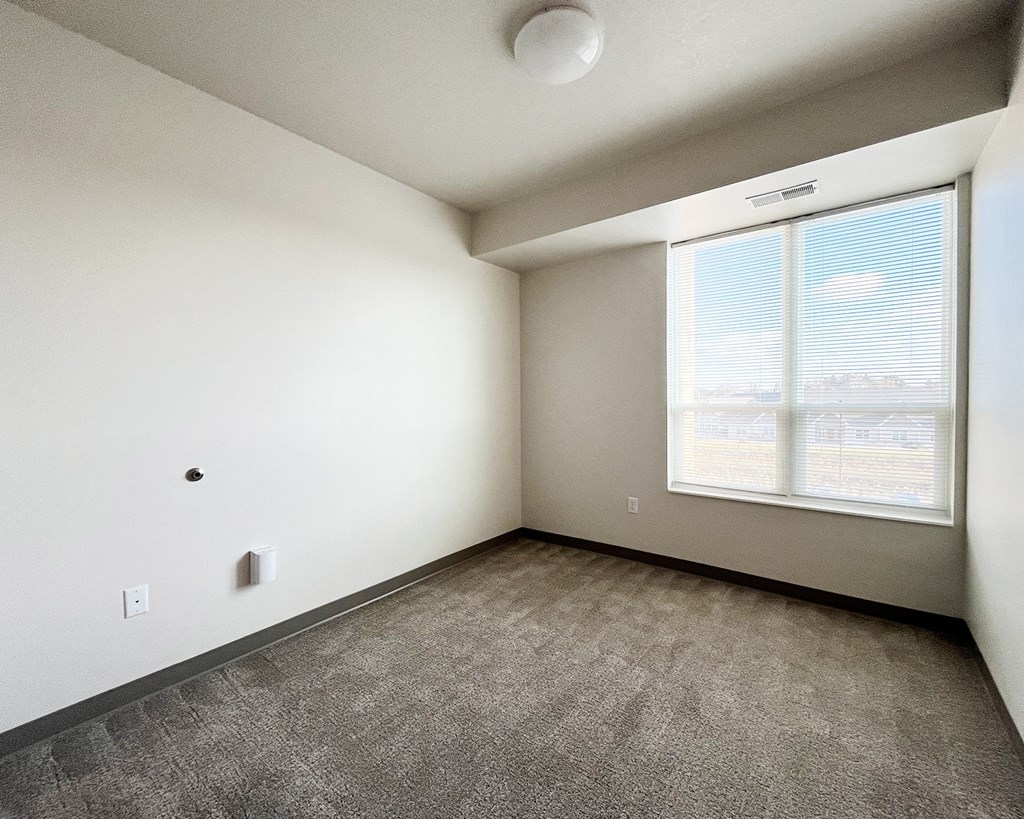 A room with a window and a grey carpet.