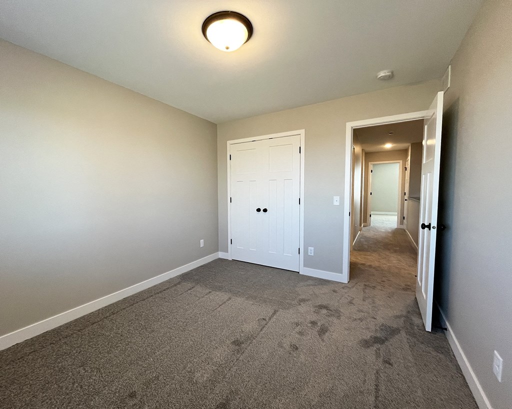an empty living room with carpet and a hallway to a bedroom