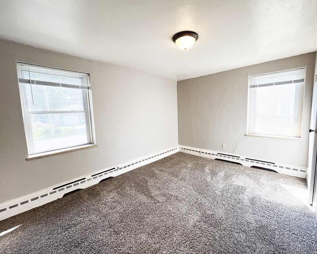 an empty room with carpet and two windows