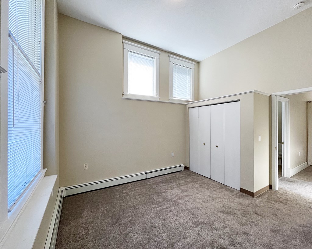 A room with a carpeted floor and a window with blinds.