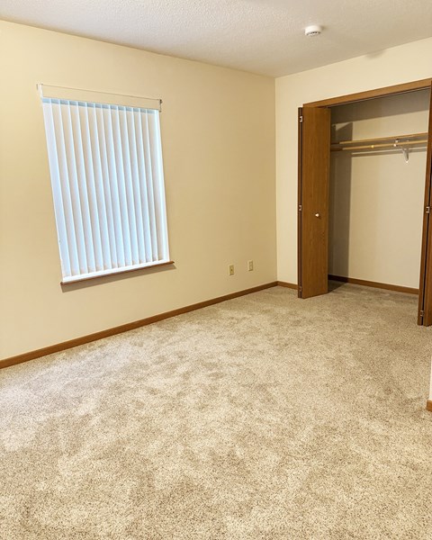 A room with a carpeted floor, a window with blinds, and a closet with a door.