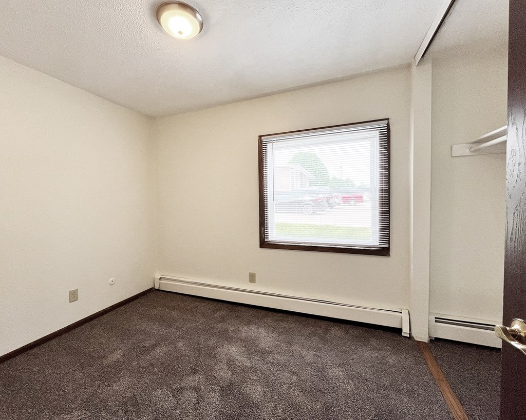 A room with a carpeted floor, a window with blinds, and a door.