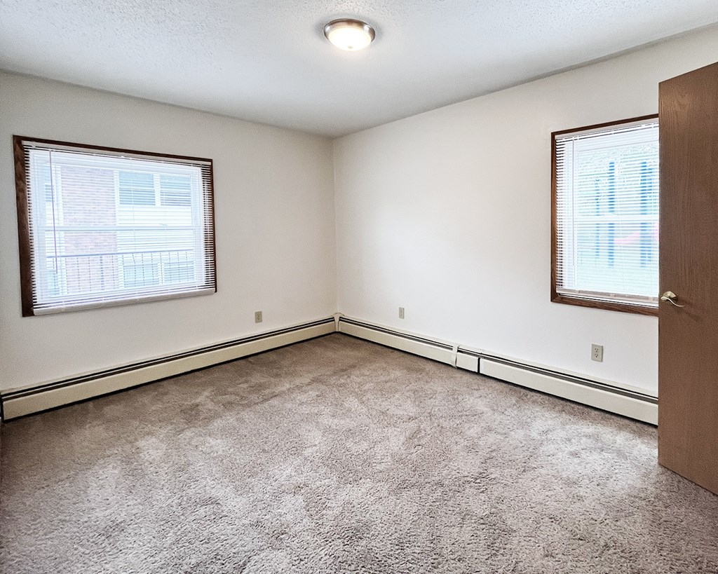 A room with a carpeted floor and two windows.