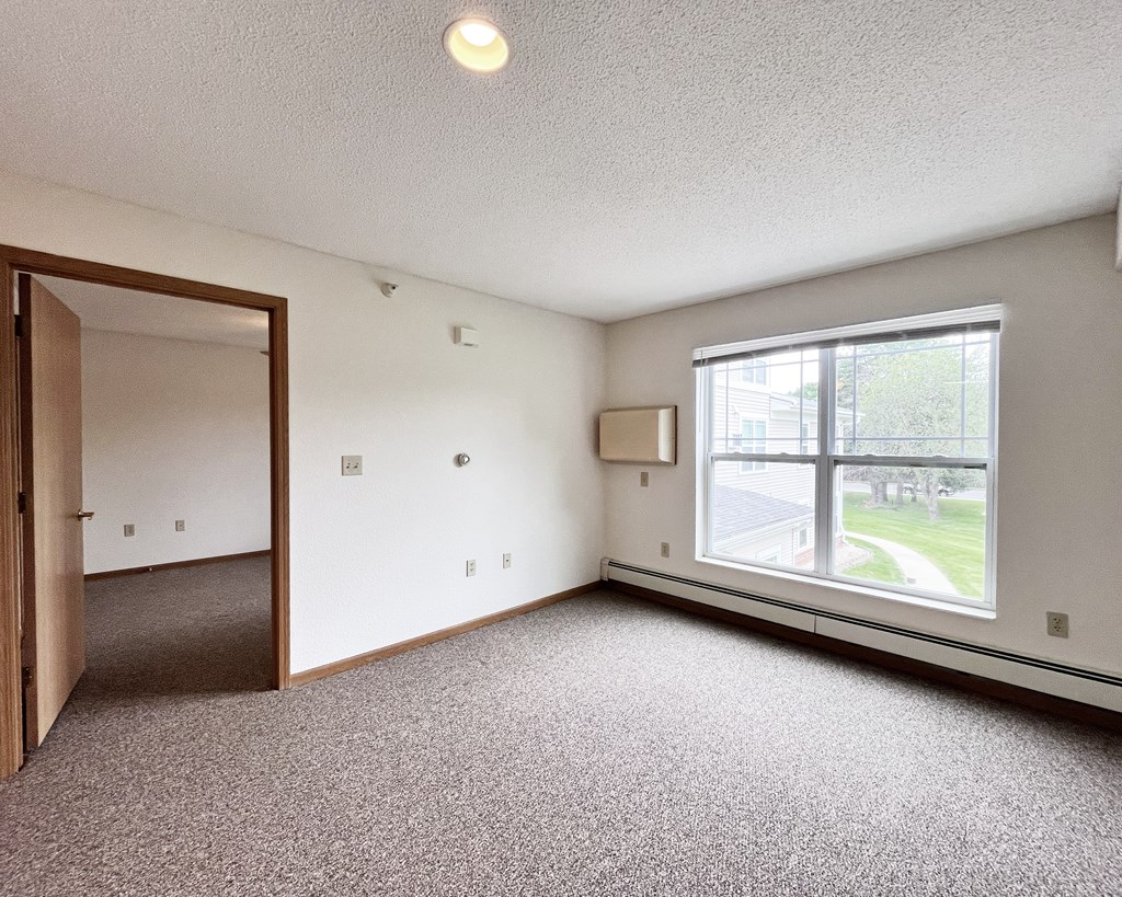 A room with a carpeted floor, a window, and a door.