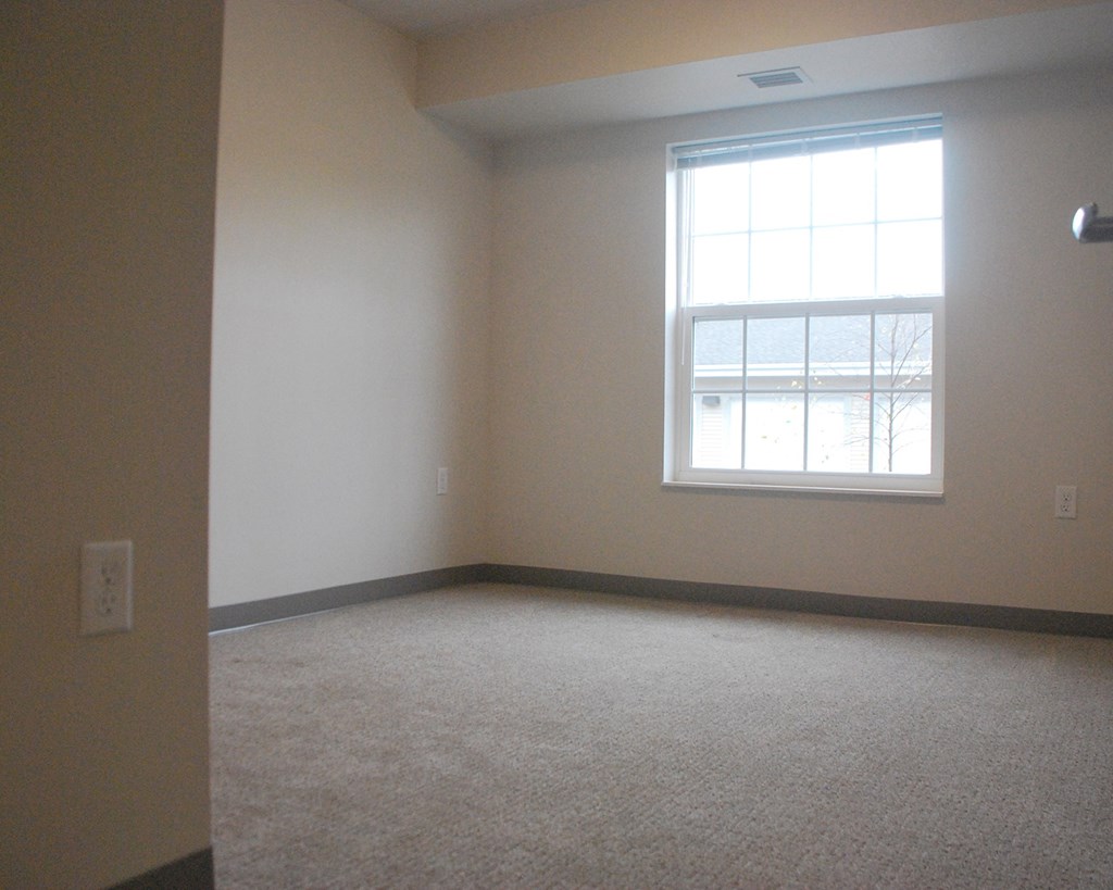 an empty living room with a window and carpet