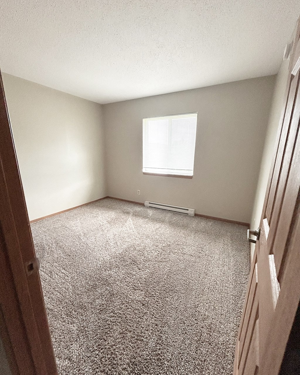 A room with a carpeted floor and a window with blinds.