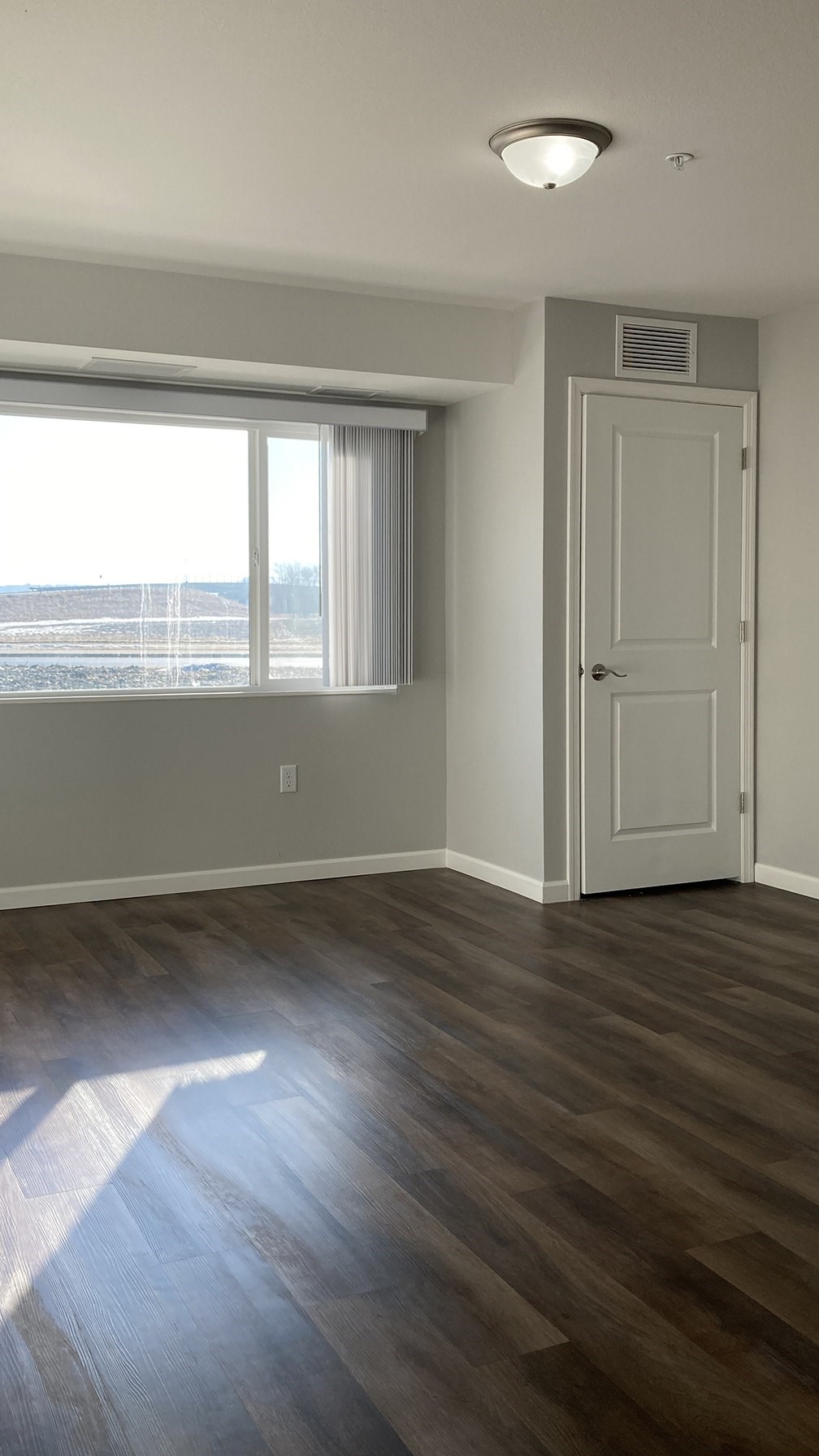 A room with a white door and a window with a view of a fence and trees.