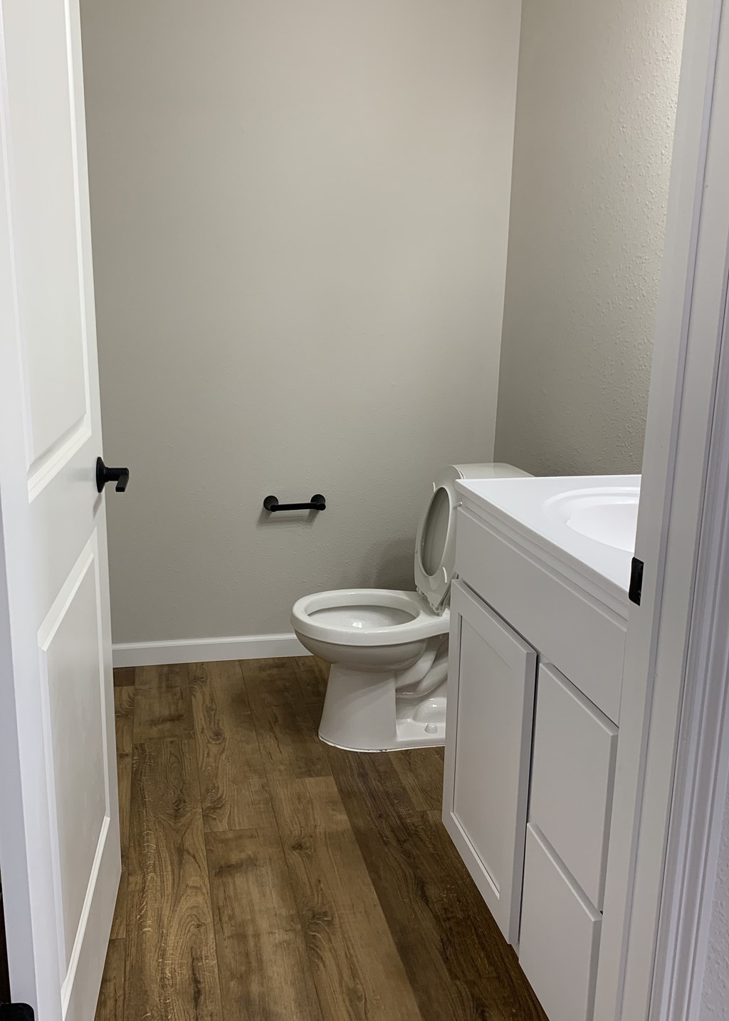 A white toilet in a small bathroom with wood flooring.