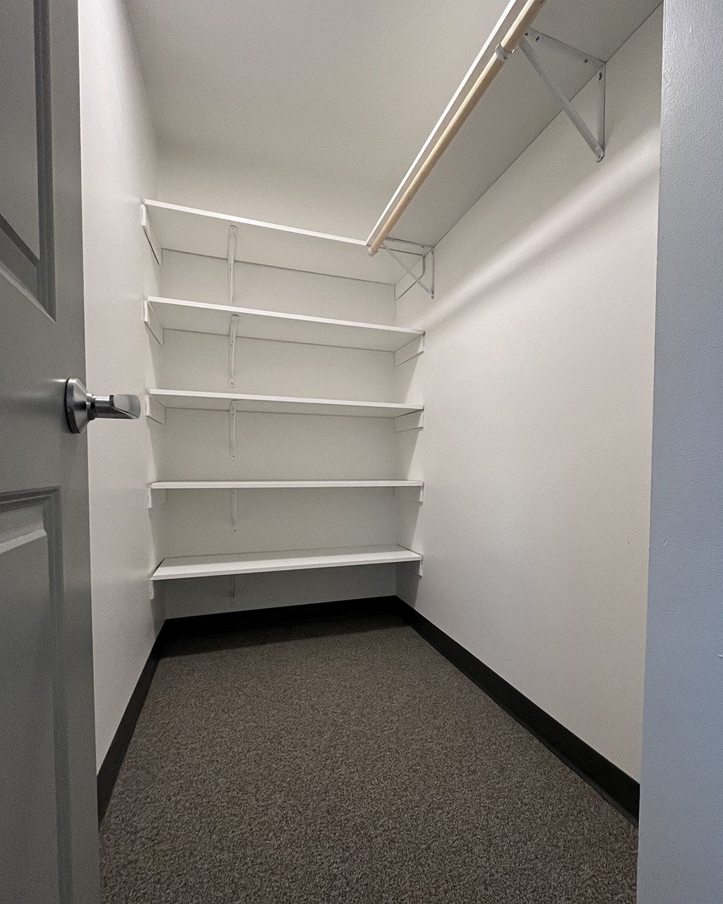 a walk in closet with white shelves and a door