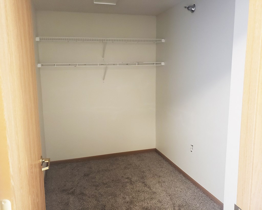 an empty closet with a white wall and a hanging rack