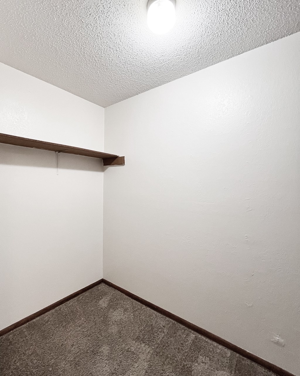 A white wall with a brown shelf and a brown floor.