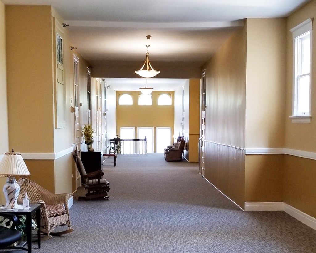 A long hallway with a lamp and chairs on the left side.
