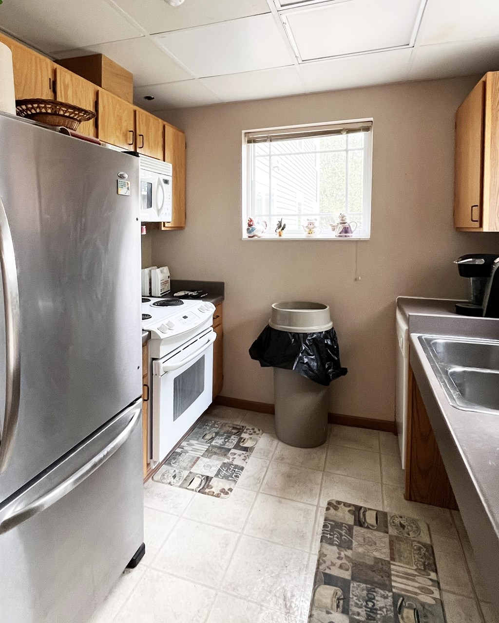 A kitchen with a stainless steel refrigerator and a window with a view of trees.