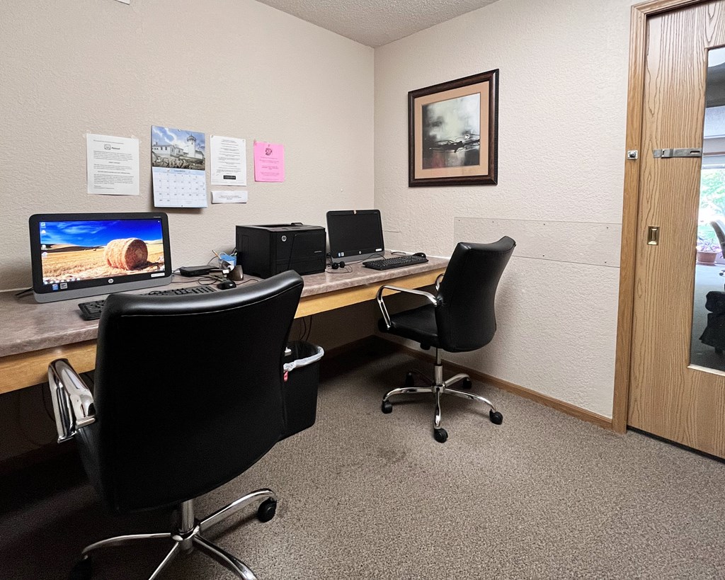 A room with a desk, chairs, and computers.