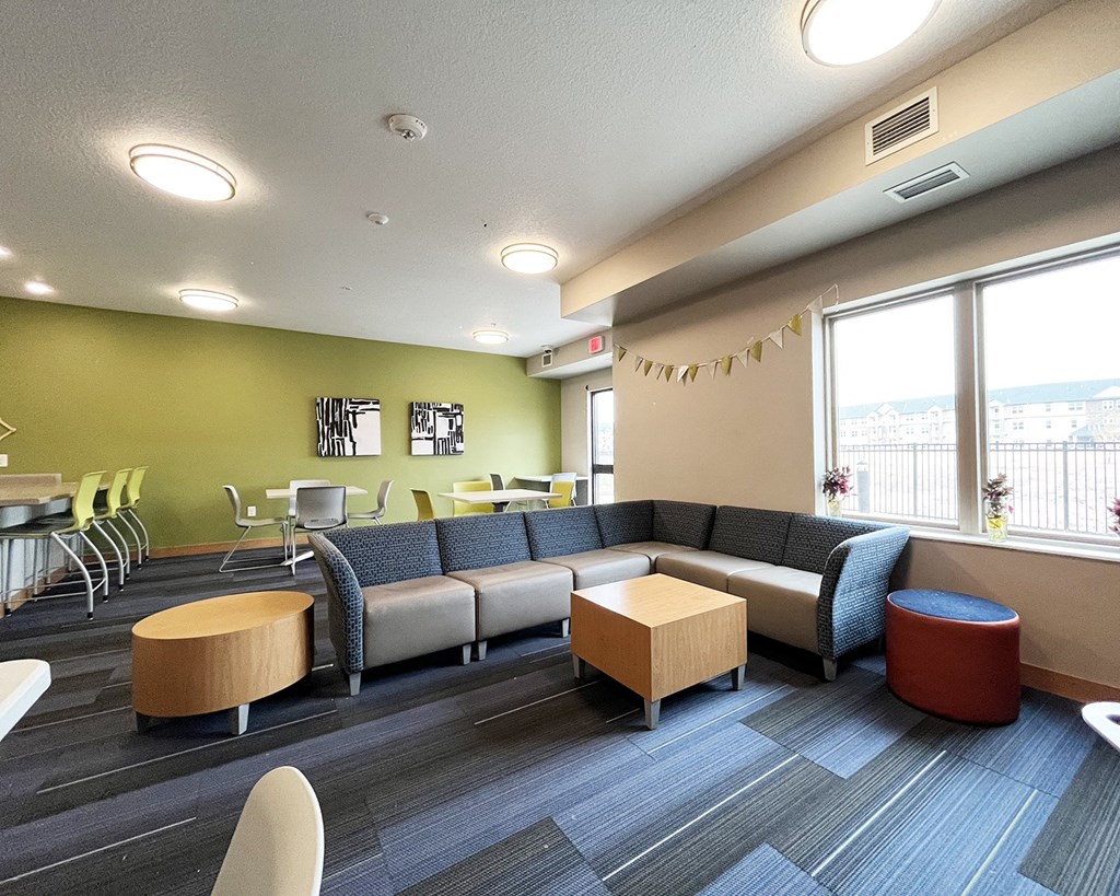 A room with a grey couch, a wooden table and a red ottoman.