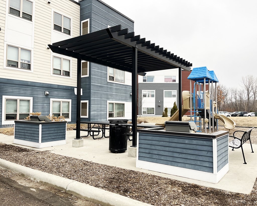A playground area with a slide and a canopy is located in front of a building.