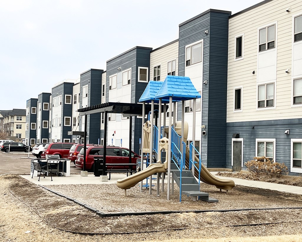 A playground with a blue roof and a yellow slide is in front of a building.