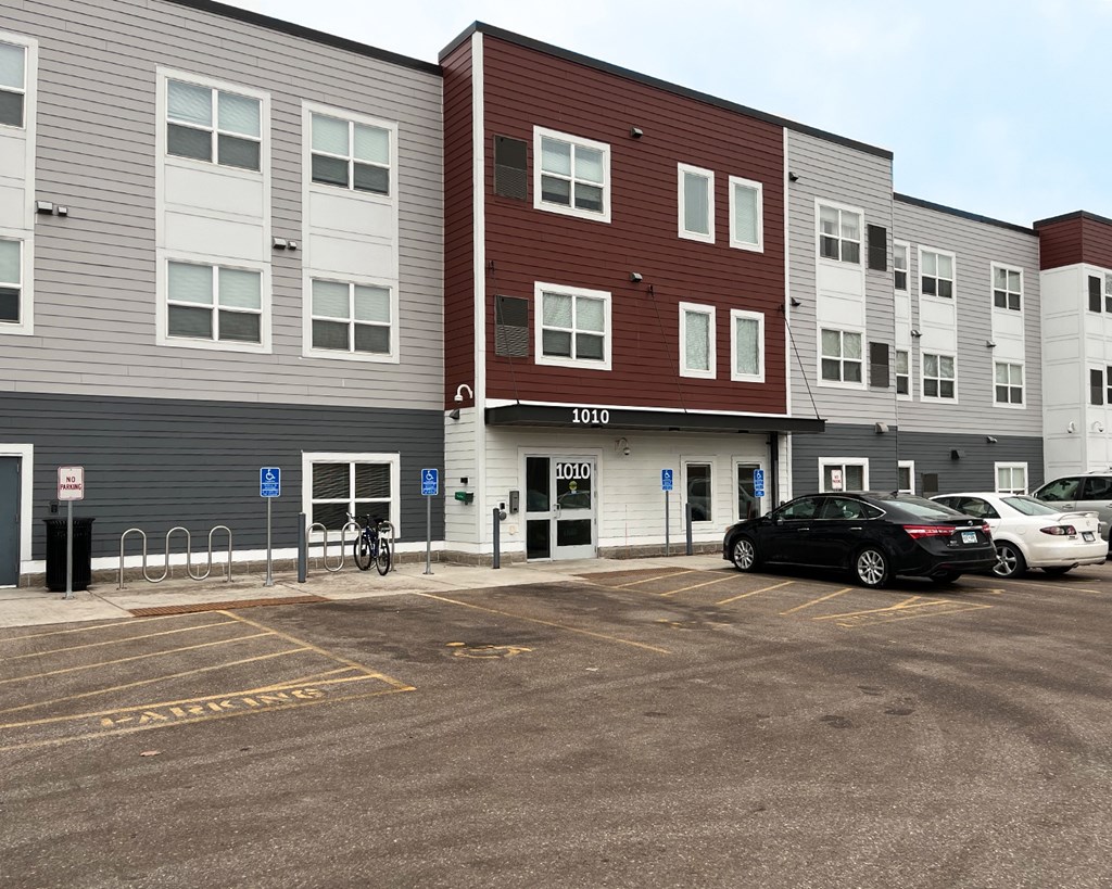 A parking lot in front of a multi-story apartment building with a black car parked in the lot.