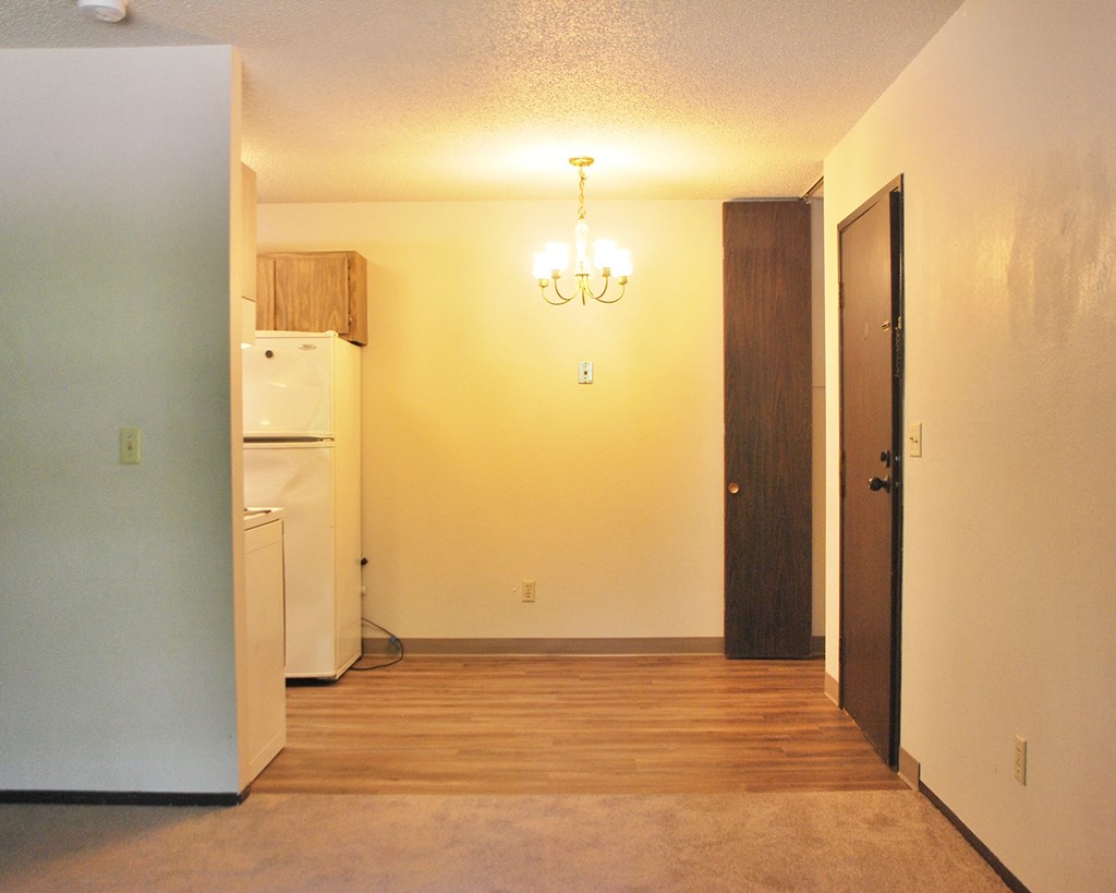 an empty living room with a refrigerator and a door