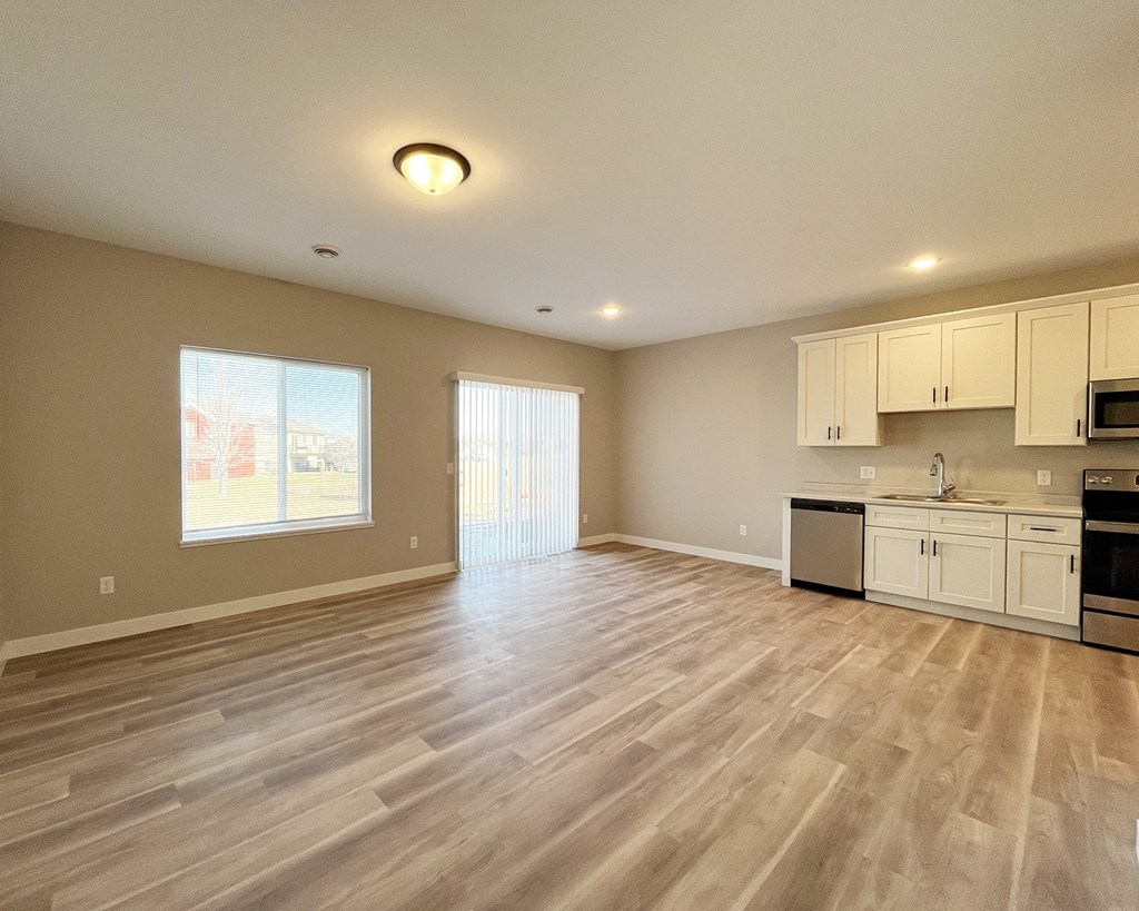 the spacious living room and kitchen of a new home with wood flooring
