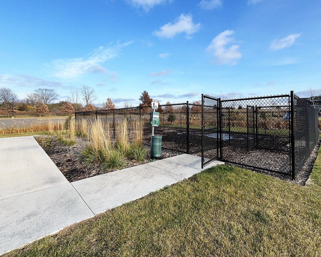 A black fence surrounds a green trash can in a grassy area.