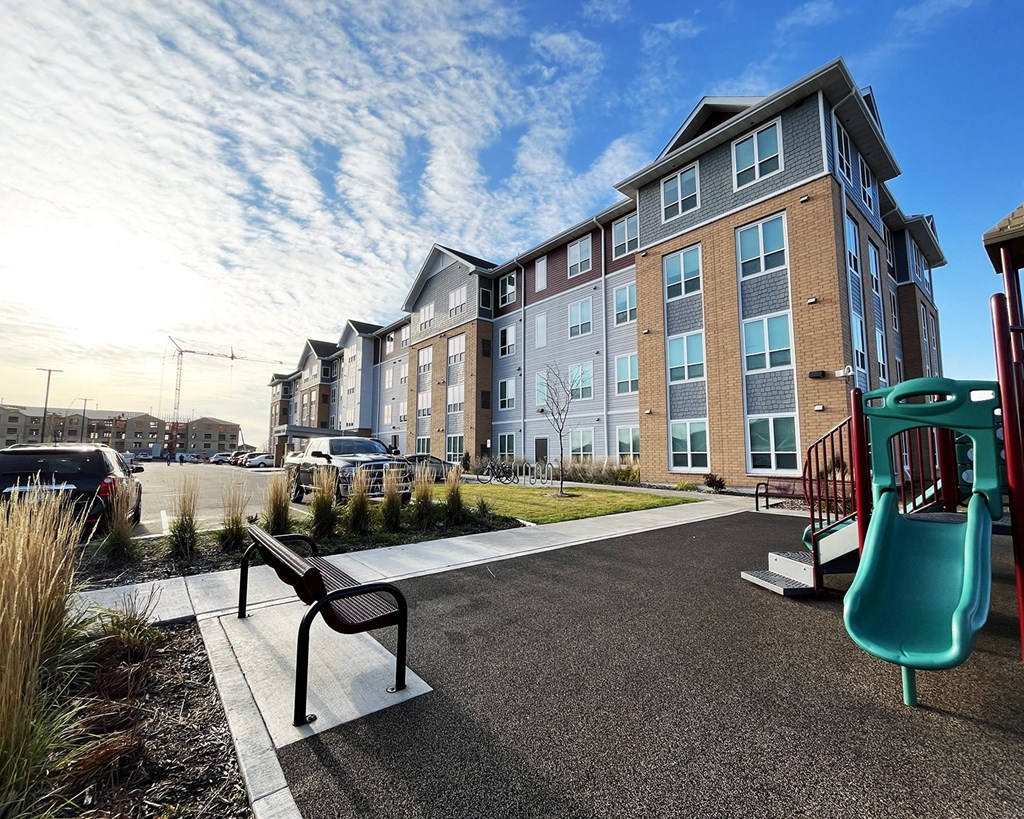 A playground with a slide and a bench in front of a building.