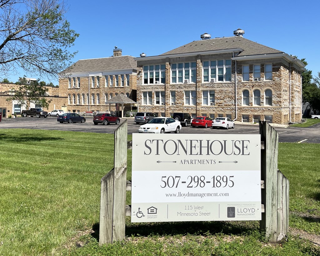 A sign for Stonehouse Apartments is in front of a brick building.