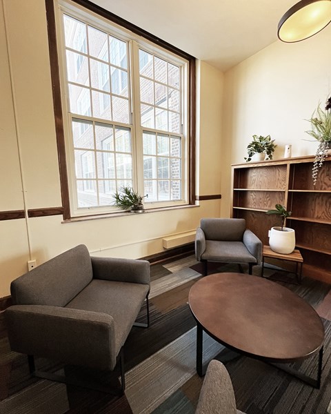 A living room with a grey couch, a brown table, and a window.