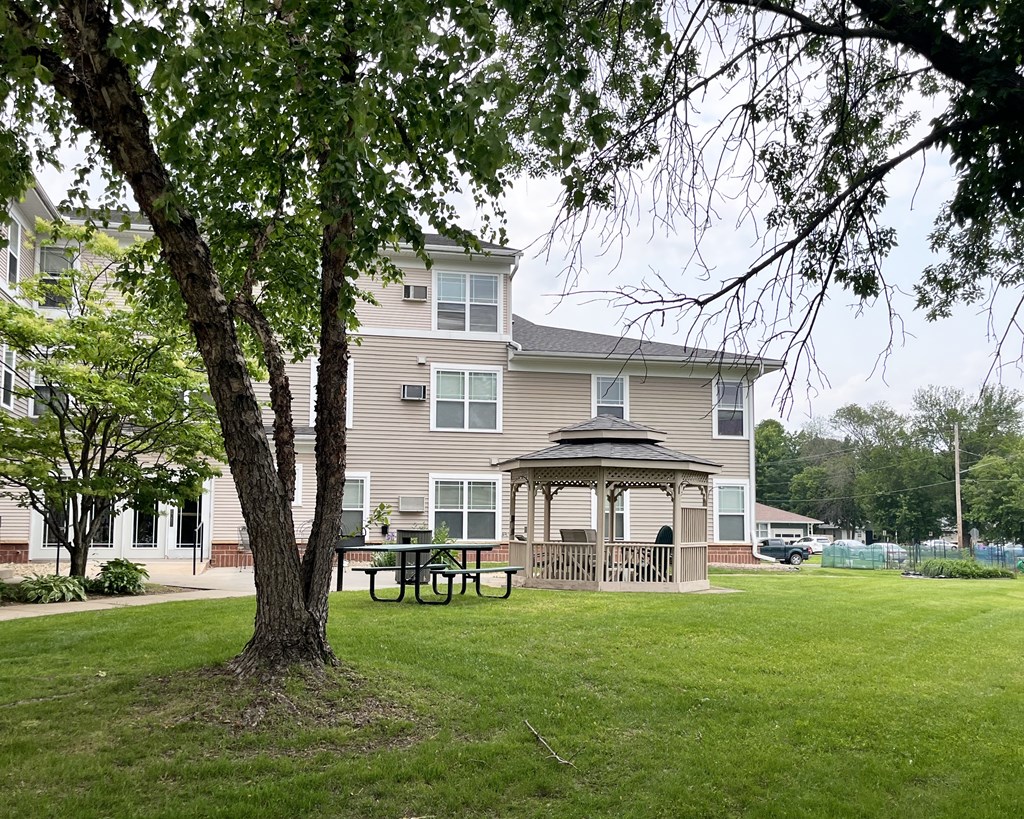 A tree stands in front of a building with a gazebo in the front yard.
