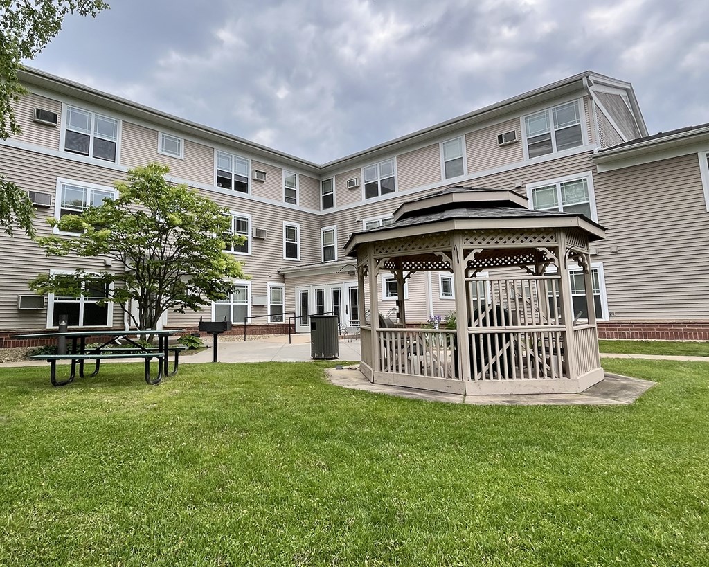 A gazebo sits in the middle of a grassy area in front of a building.