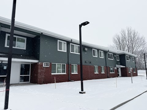 A building with a grey roof and red brick walls is surrounded by snow.