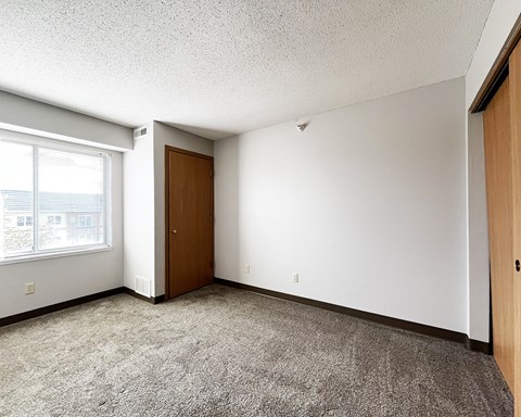 A room with a carpeted floor, a brown door, and a window with blinds.