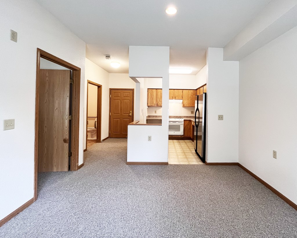 A white kitchen with a white island in the middle of a hallway.