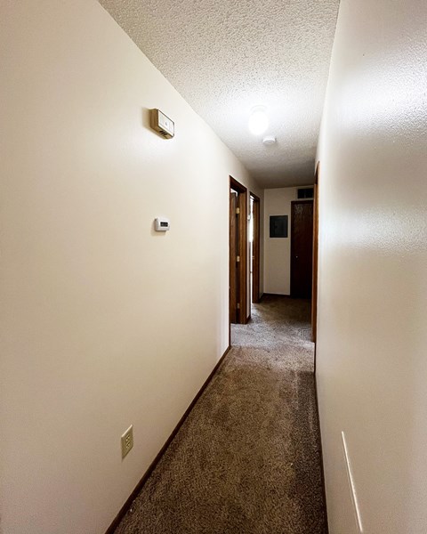 a hallway with white walls and a carpeted floor and a door to a room