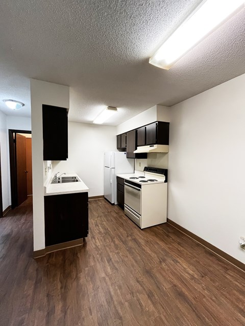 A kitchen with white appliances and brown floors.