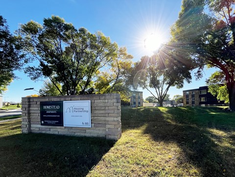 A sign for Homestead Housing Partnership stands in front of a grassy area.