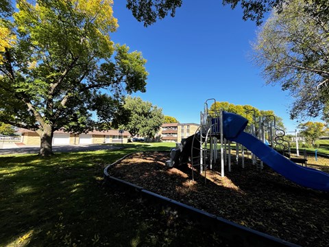 A playground with a blue slide and a tree with yellow leaves.