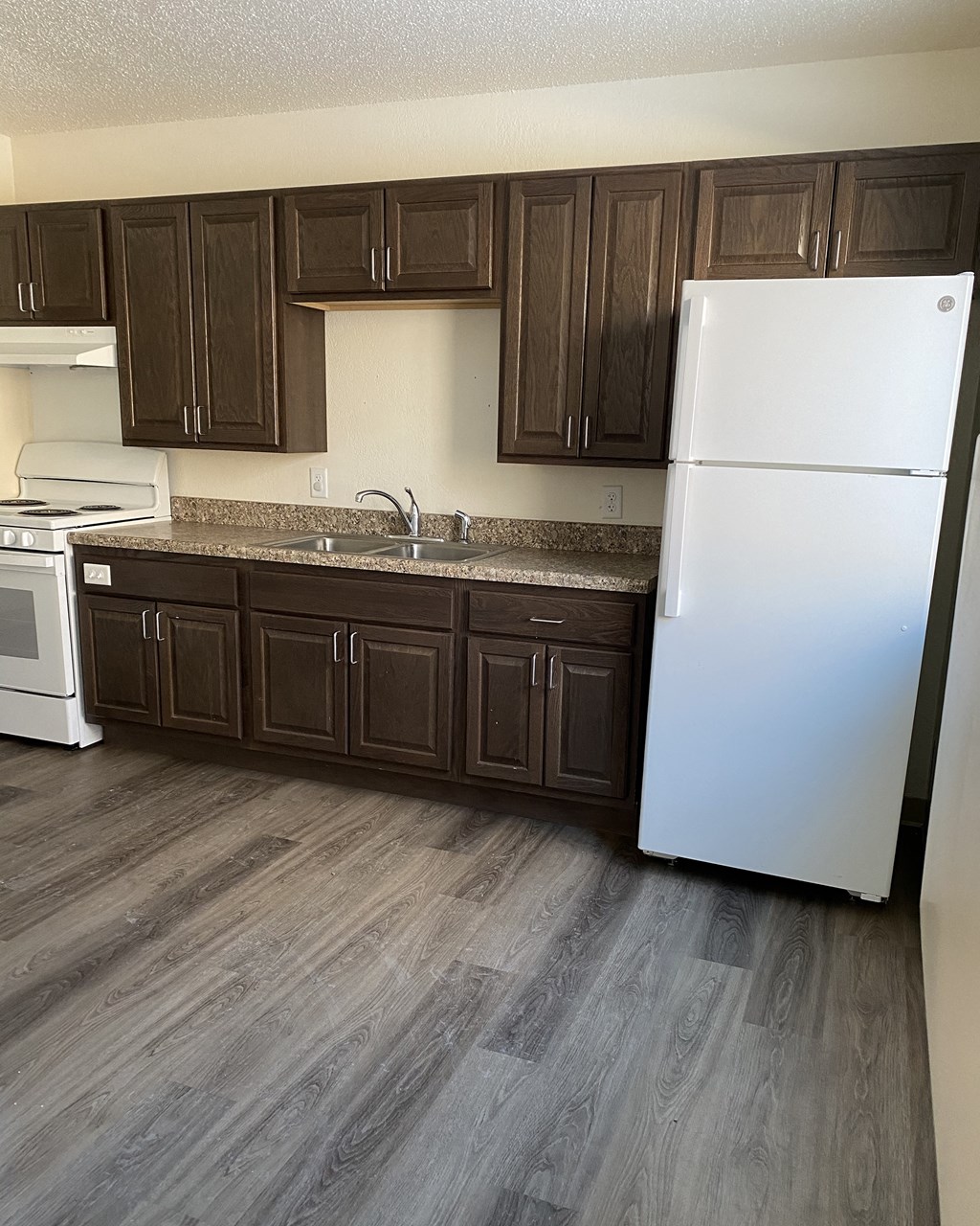 an empty kitchen with dark cabinets and a white refrigerator