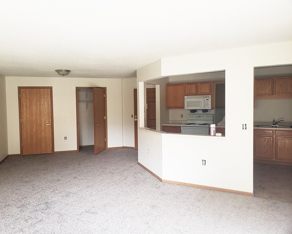 an empty living room with a kitchen and a door to a hallway